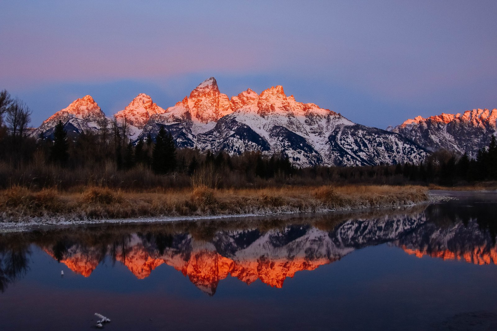 The Teton range reflected in still water at Schwabacher Landing at sunrise